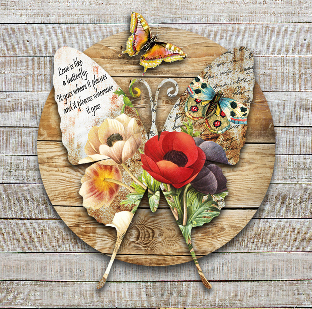 Vintage Butterfly Dimensional Metal Wall Décor by Ralph Burch is pictured here with a background of weathered wood. raised and attached to the background is a Butterfly shape which has a floral and butterfly image on it. On one wing it says Love is like a Butterfly, It goes where it pleases and pleases where it goes!. And avove that also attached to the background is a raised butterfly. 2 pieces of metal complete the piece.