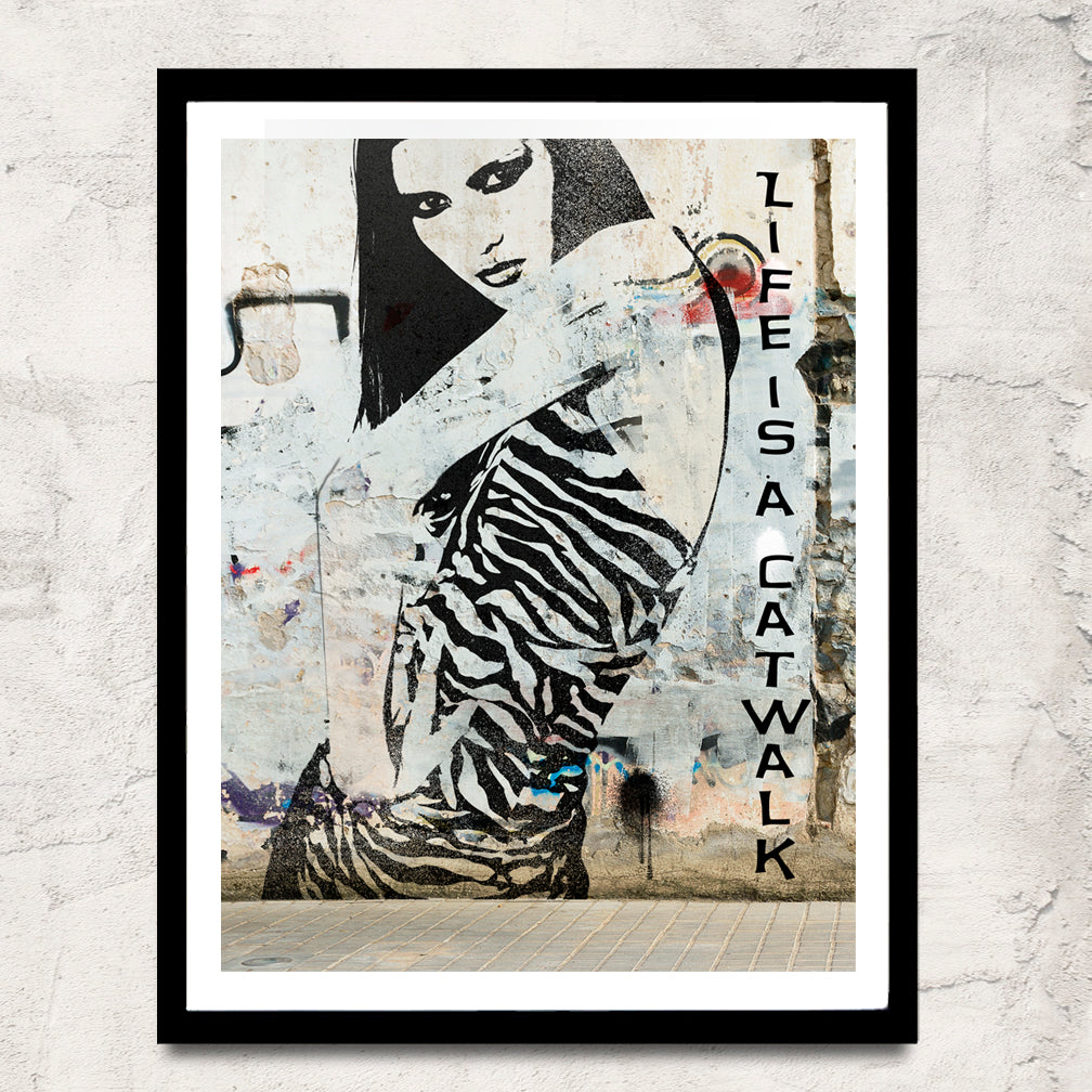 Life is a Catwalk is a black Graphic of a Fashion model in a pose painted on the side of a building an the photographed depicting how we are constantly judged out in public by Ralph Burch shown in a floater frame