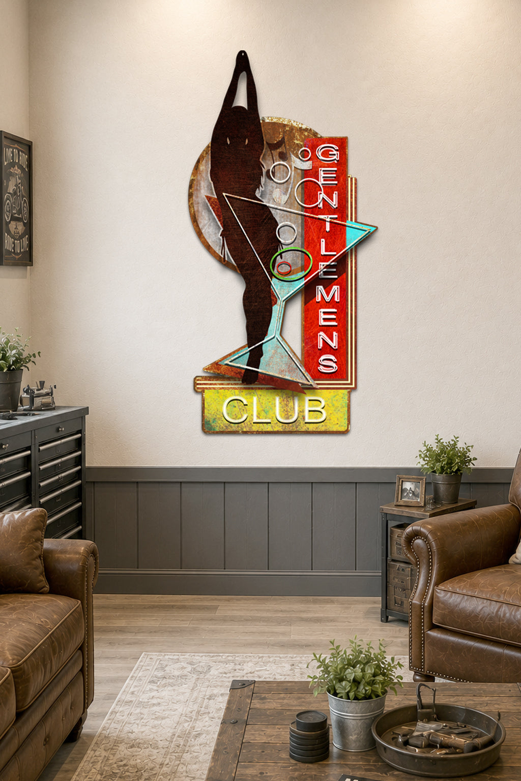 A vintage-style wall art piece featuring a martini glass silhouette with the words 'GENTLEMEN CLUB' in red, yellow, white, and teal, displayed on a beige wall in a living room setting.
