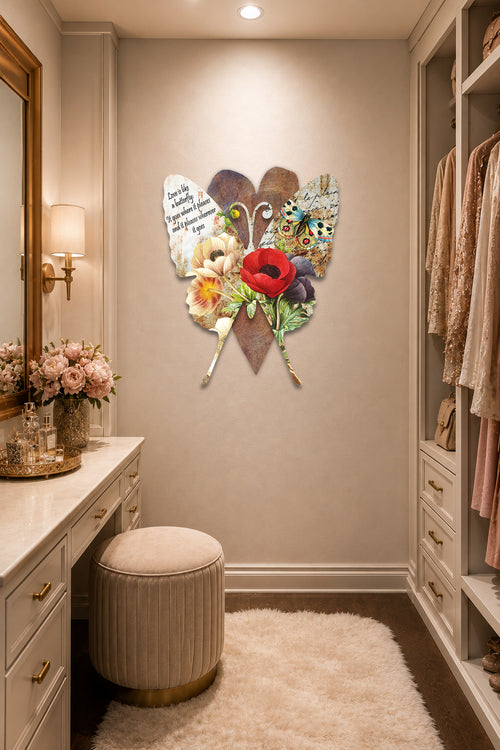 A decorative wall art piece featuring a butterfly made from layered leaves, feathers, and colorful flowers, displayed in a styled walk-in closet or dressing area with a vanity, stool, rug, and hanging garments.