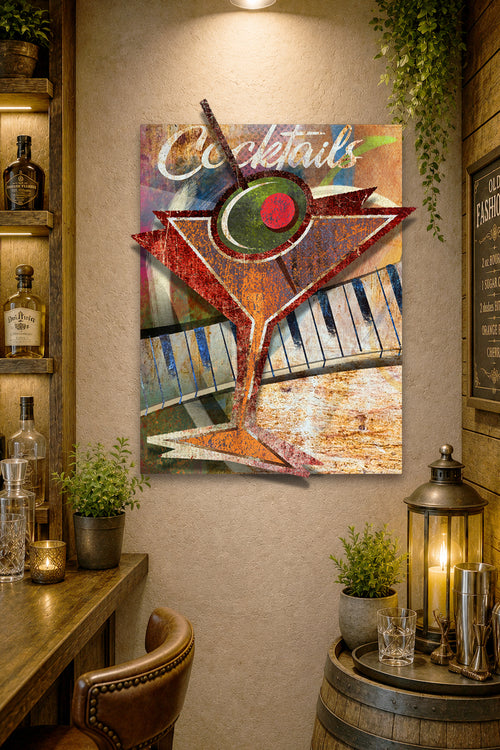 A rectangular wall art print featuring a stylized martini glass with piano keys and the word 'Cocktails' in script, displayed in a rustic bar-themed room with bottles, plants, and a lantern.
