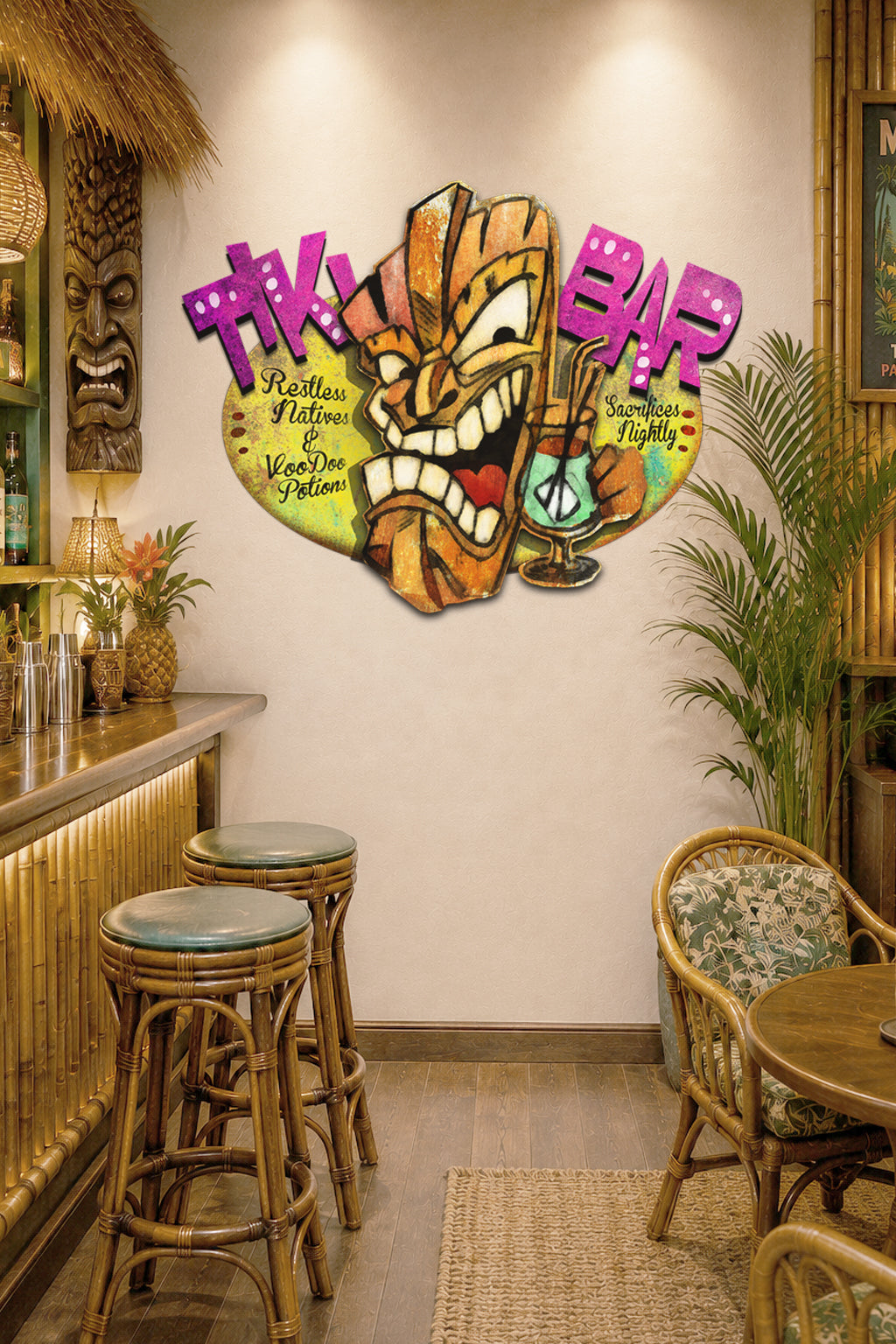 A tropical-themed wall decal featuring a carved tiki mask and the words 'Tiki Bar' in pink and purple lettering, displayed on a beige wall in a bar interior setting.