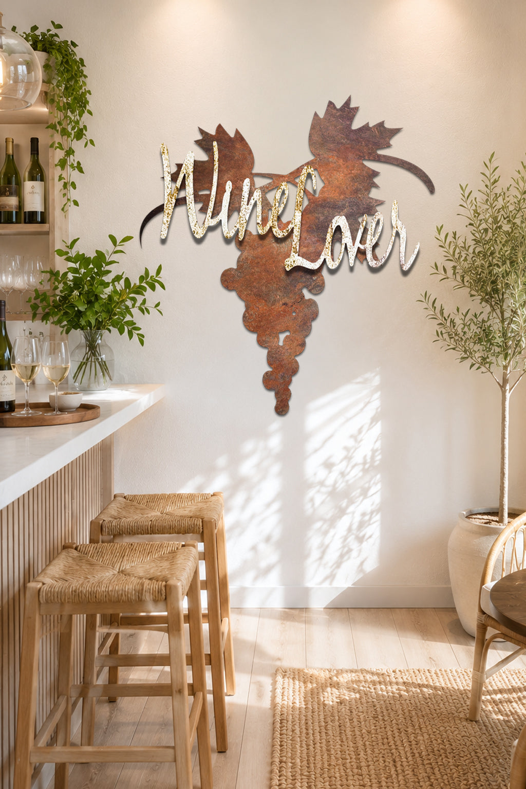 Rustic metal wall art featuring a grapevine silhouette and the words 'Wine Lover' in white script, displayed on a light wall in a bright, modern kitchen or bar setting with wooden stools and plants.